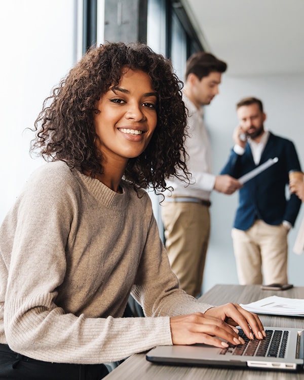 African-American woman smiling while sitting in the office on her laptop