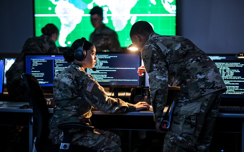 Male and female soldiers in uniform in a control room reviewing information